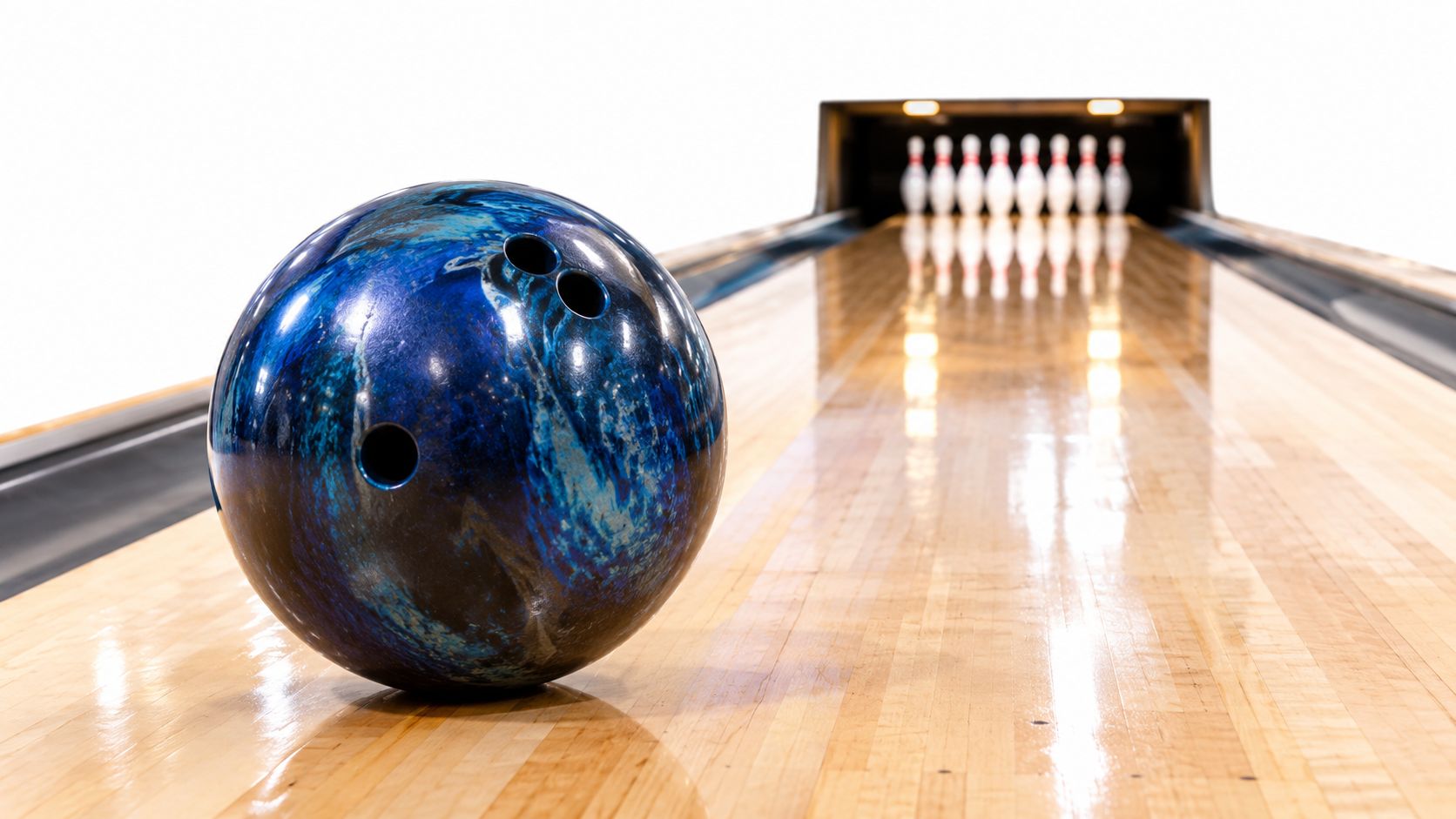 A glossy blue and black marble-patterned bowling ball sits on a wooden bowling lane facing pins.