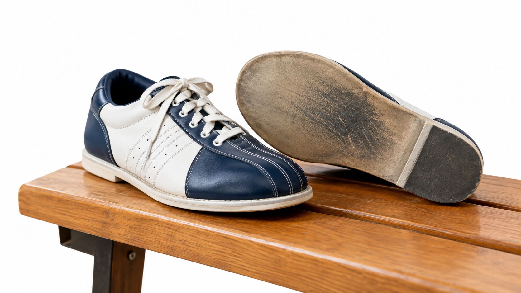 A pair of blue and white leather bowling shoes resting on a wooden bench against white background.