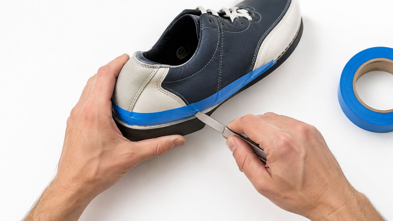 A person using a tool to carefully apply blue painter's tape along the heel of a shoe.